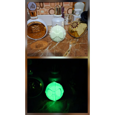 Adorno bola Navidad de cemento fosforescente con diseño de regalo y lazo de día junto a perfumes y brillo verde en la oscuridad.
