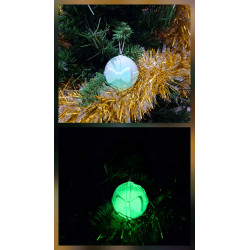 Adorno bola Navidad de cemento fosforescente con diseño de regalo y lazo de día en el abeto y brillando verde de noche.