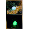 Adorno bola Navidad de cemento fosforescente con diseño de regalo y lazo de día en el abeto y brillando verde de noche.