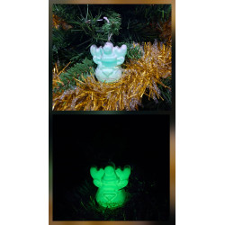 Adorno reno Navidad de cemento fosforescente con gorro de día en el abeto junto a espumillón dorado y brillando verde de noche.