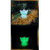 Adorno reno Navidad de cemento fosforescente con gorro de día en el abeto junto a espumillón dorado y brillando verde de noche.