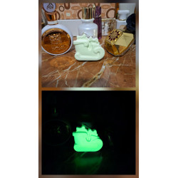 Adorno trineo Navidad de cemento fosforescente mostrando su diseño con regalos de día y su brillo verde en la oscuridad.