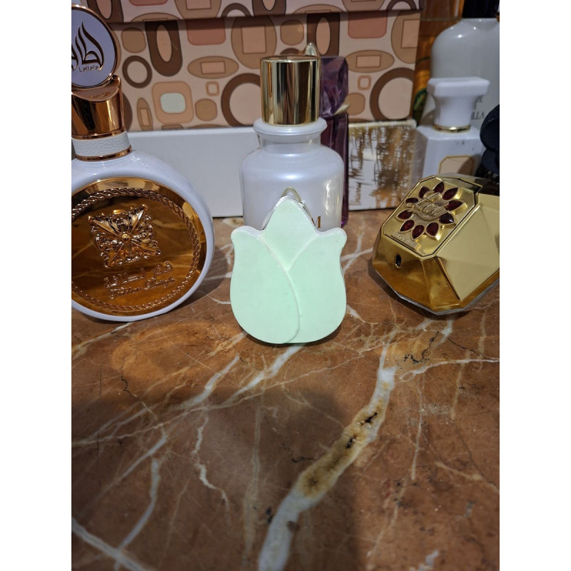 Adorno de tulipán de cemento fosforescente mostrando su diseño floral de día junto a frascos de perfume sobre mármol.