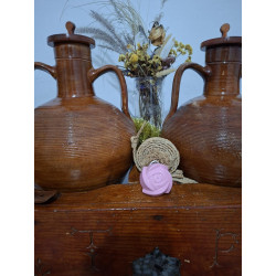 Adorno de rosa de cemento pintada a mano en color rosa colocado sobre mueble de madera entre dos vasijas de barro tradicionales.