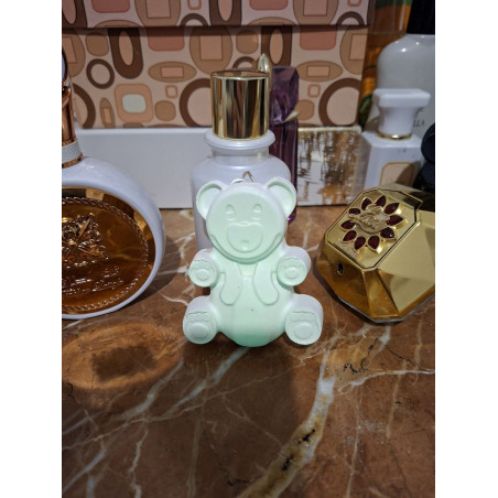 Adorno osito de cemento fosforescente estilo gominola colocado de forma horizontal en un tocador junto a perfumes sobre mármol.