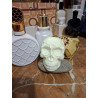 Adorno de calavera de cemento fosforescente con corona de espinas de día apoyada en una piedra junto a perfumes sobre mármol.