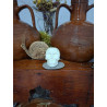 Adorno de calavera de cemento fosforescente de día apoyado sobre una piedra en un mueble de madera entre dos vasijas de barro.