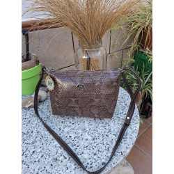Bolso bandolera de piel legítima con grabado de serpiente metalizado en tonos marrones sobre una mesa de granito de exterior.