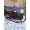 Bolso cruzado de cuero acharolado oscuro con relieve de escamas brillantes y correa ajustable fabricado en España.
